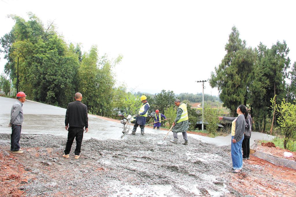 修路：钟德琼（右一）在公路硬化现场进行质量监督